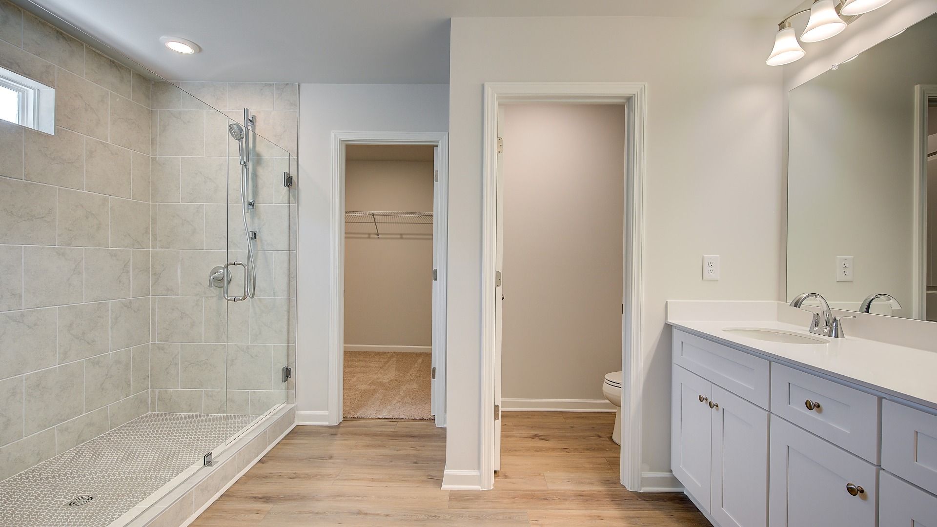 Luxury primary bath with dual vanities and elegant tile floors, and walk-in shower in the Wagener at Bowers Farm.