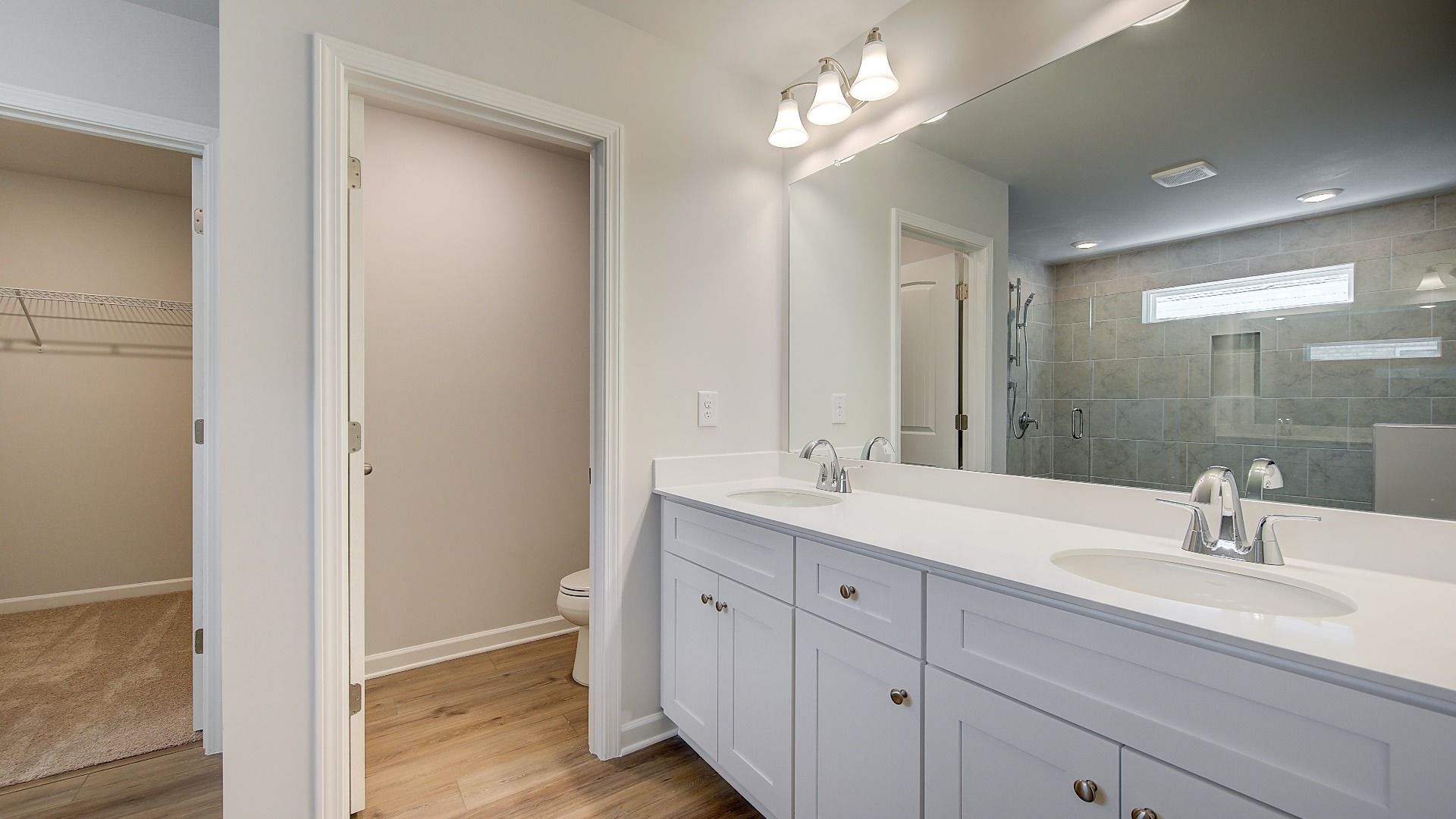 Luxury primary bath with dual vanities and elegant tile floors, and walk-in shower in the Wagener at Bowers Farm.