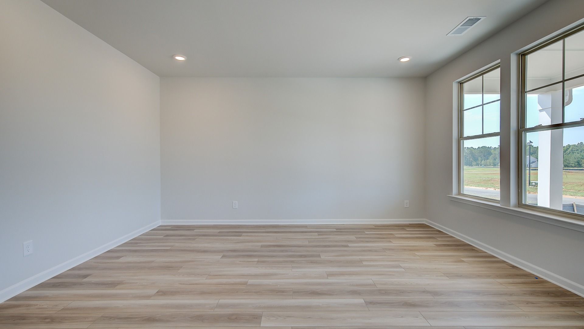 Bright living room with LVP flooring and large windows in the Clarity at Brighton in Locust Grove, GA.