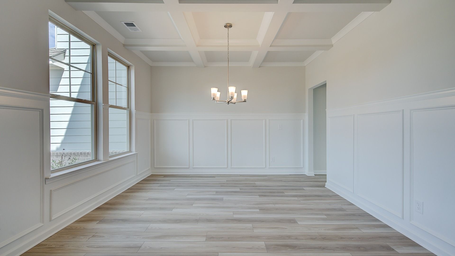 Open dining room with coffered ceiling, chandelier lighting, and LVP flooring in the Clarity at Brighton in Locust Grove, GA.