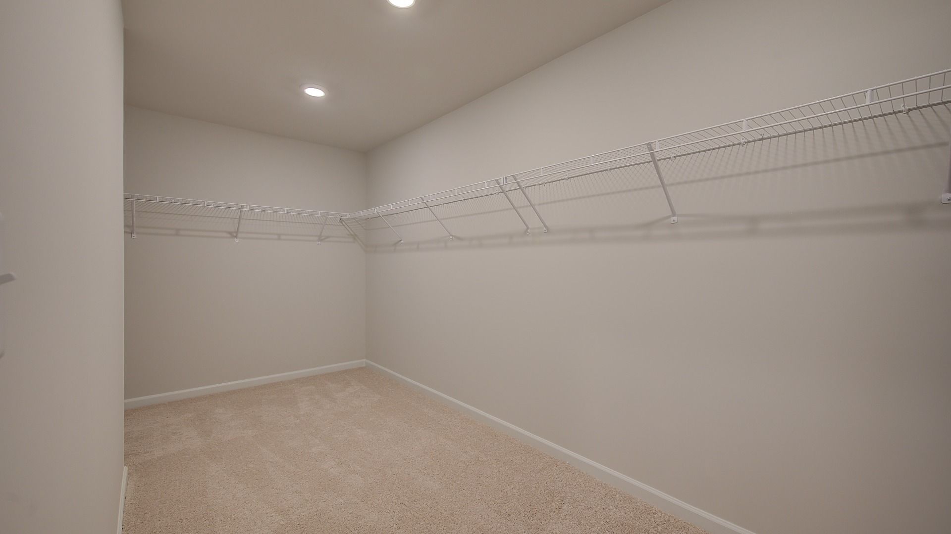 Primary closet connected to bath with carpet flooring and built-in shelving in the Clarity at Brighton in Locust Grove, GA.