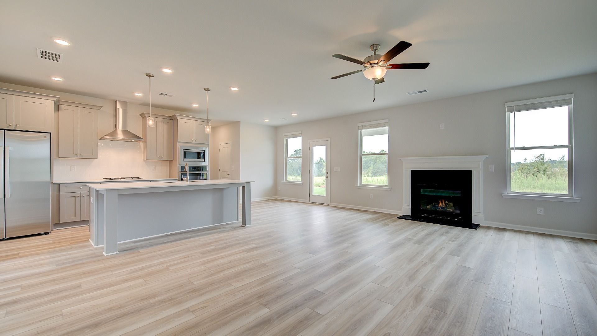 Meridian II open-concept family room with gas fireplace, LVP flooring, and kitchen view at Brighton in Locust Grove, GA.