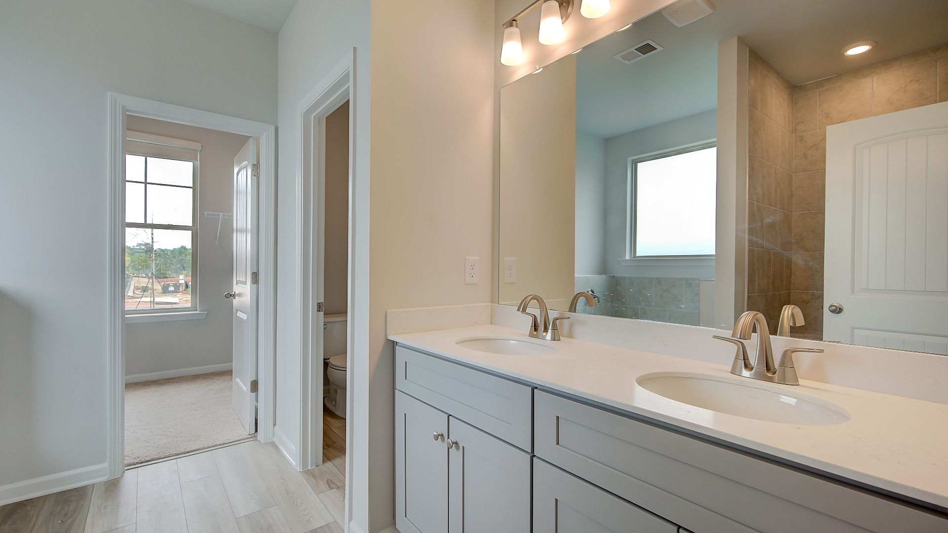 Meridian II primary bath with dual vanities and modern tile flooring, shower, and bath surround at Brighton.
