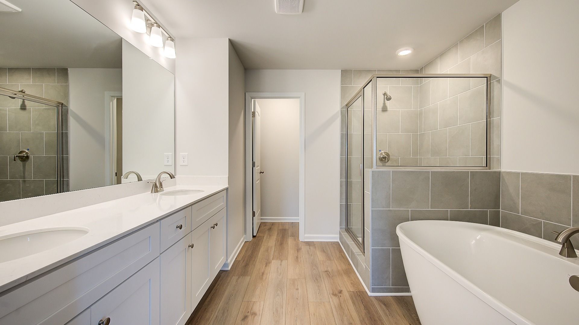 Meridian II primary bath with dual vanities and modern tile throughout floors, tub surround, and walk-in shower at Brighton.