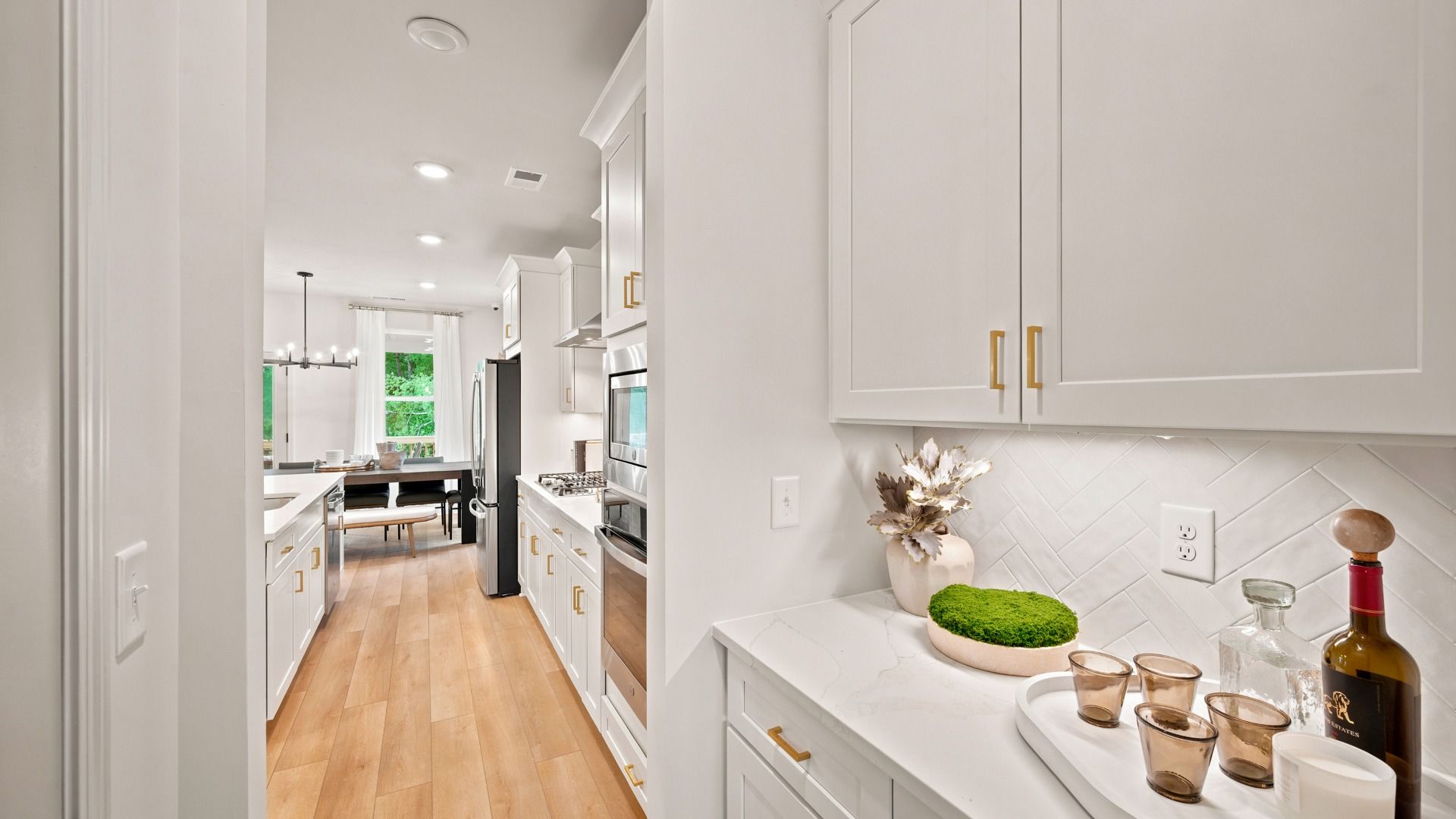 Rosemary II kitchen featuring neutral tile backsplash, white cabinetry, and stainless steel appliances at Brighton.