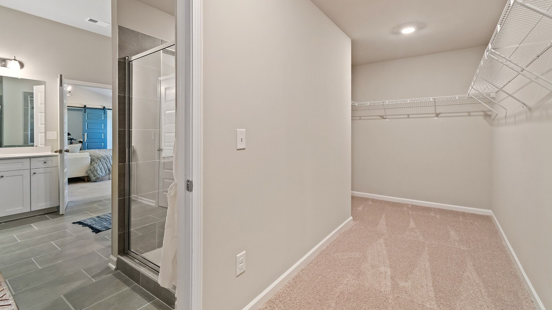 Primary walk-in closet attached to primary bath with carpet flooring and built-in shelving in the McKinley II at Brighton.