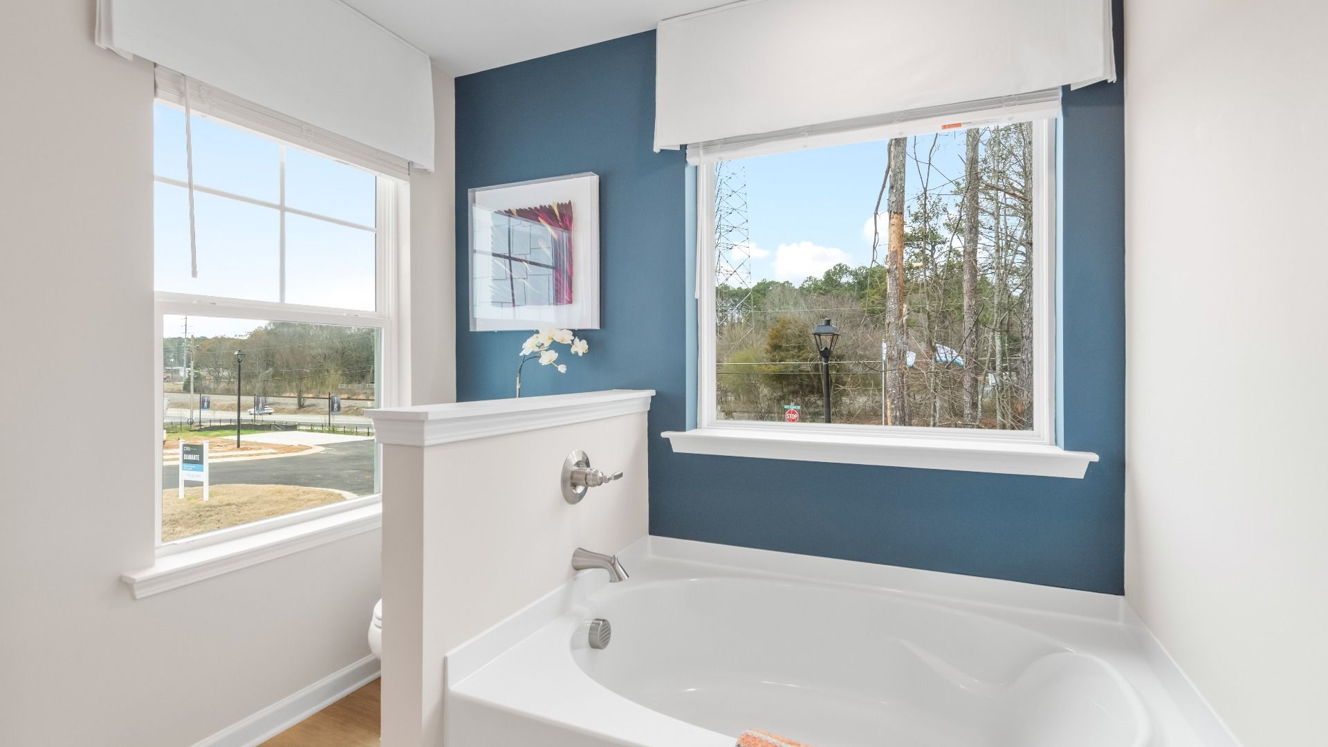 Soaking tub in primary bathroom with large windows, blue accent wall, and natural light in Diamante in Stockbridge, GA.
