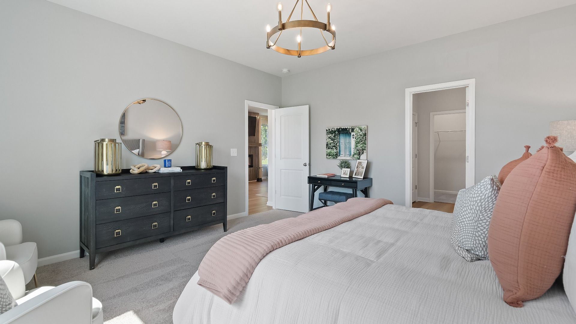 Generously-sized primary suite on main floor of Millhaven at Abbotts Crossing featuring carpet flooring.