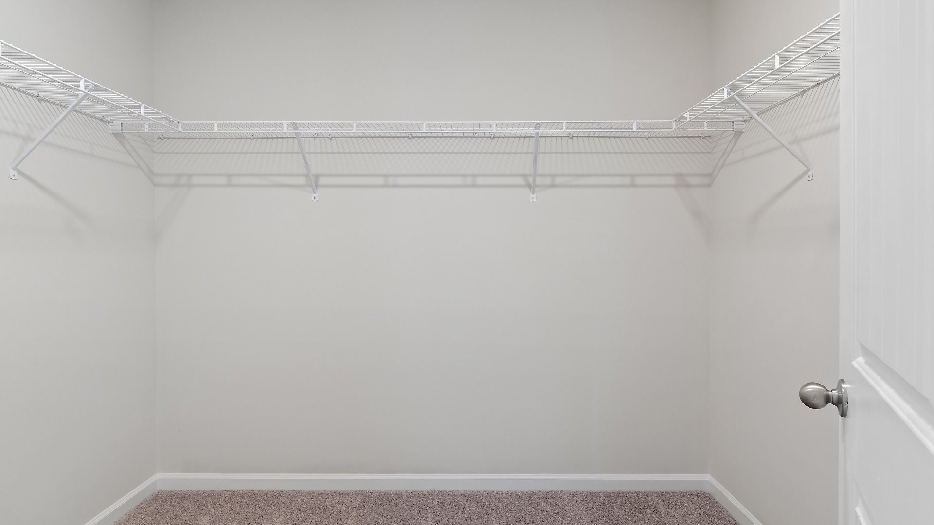 Spacious primary closet with built-in shelves for storage and carpet flooring in Millhaven plan at Abbotts Crossing.