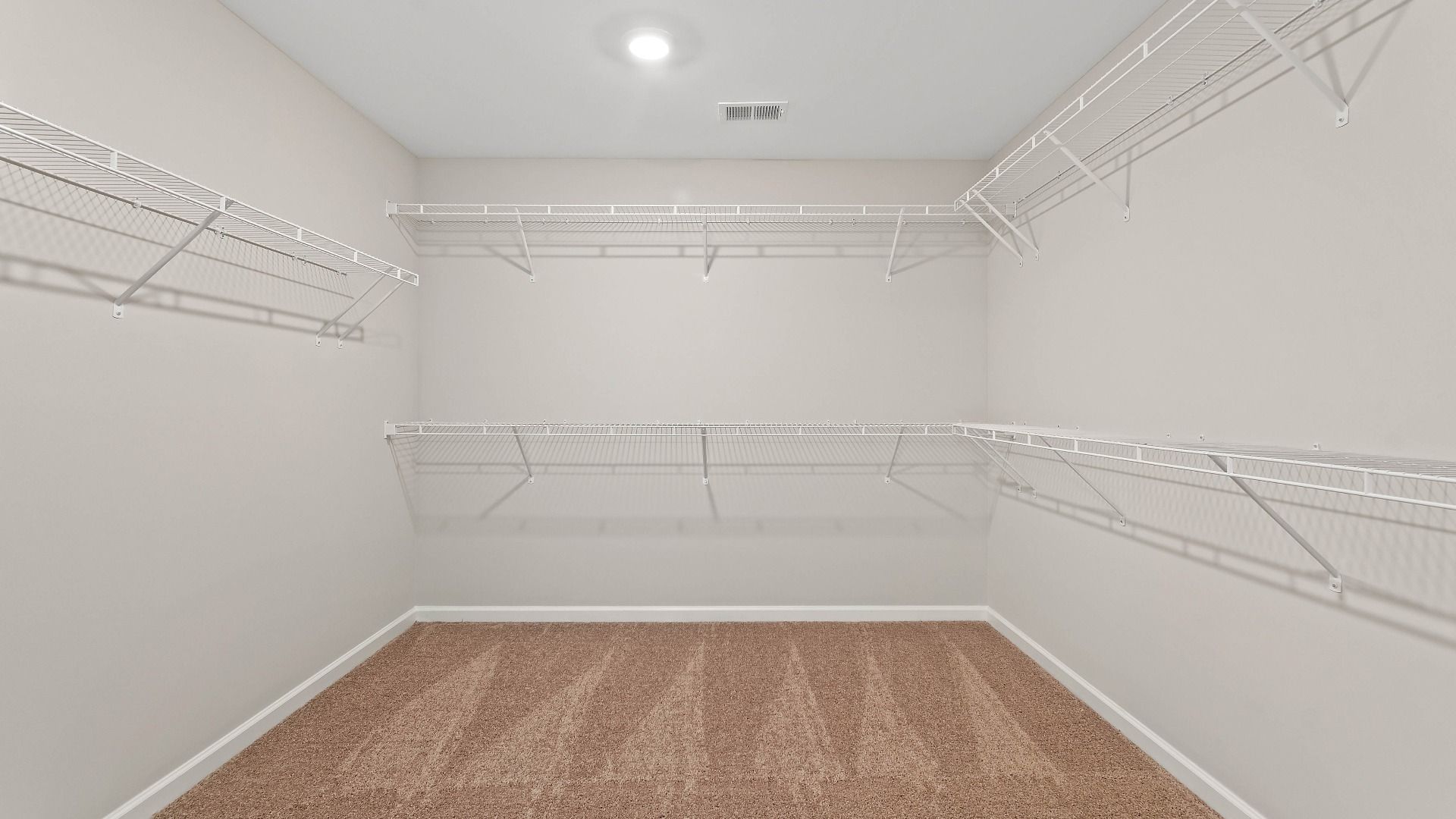 Generously-sized primary closet with carpet flooring and built-in shelves for storage in the Isabella II at Adagio.