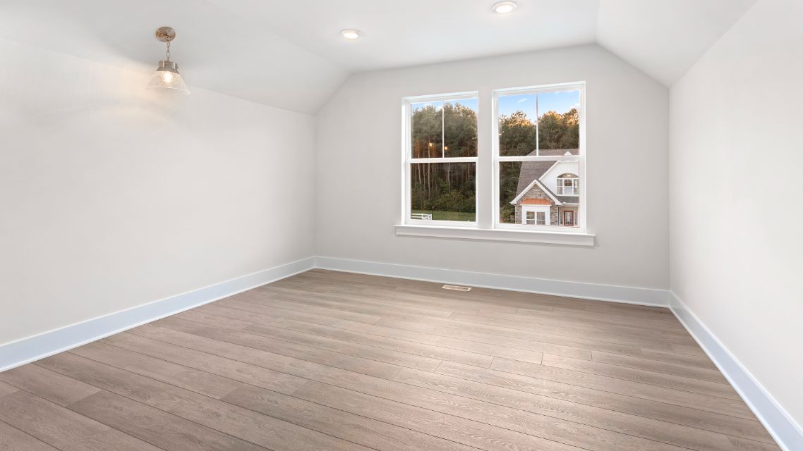 Upper bonus room with large double window, wood floors and vaulted ceiling in a DRB Homes Latitude home.