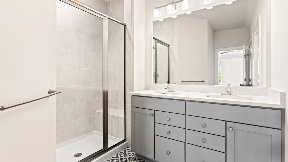 Owner's bathroom with gray, dual sink vanity and walk-in, tiled shower in a DRB Homes Latitude home.