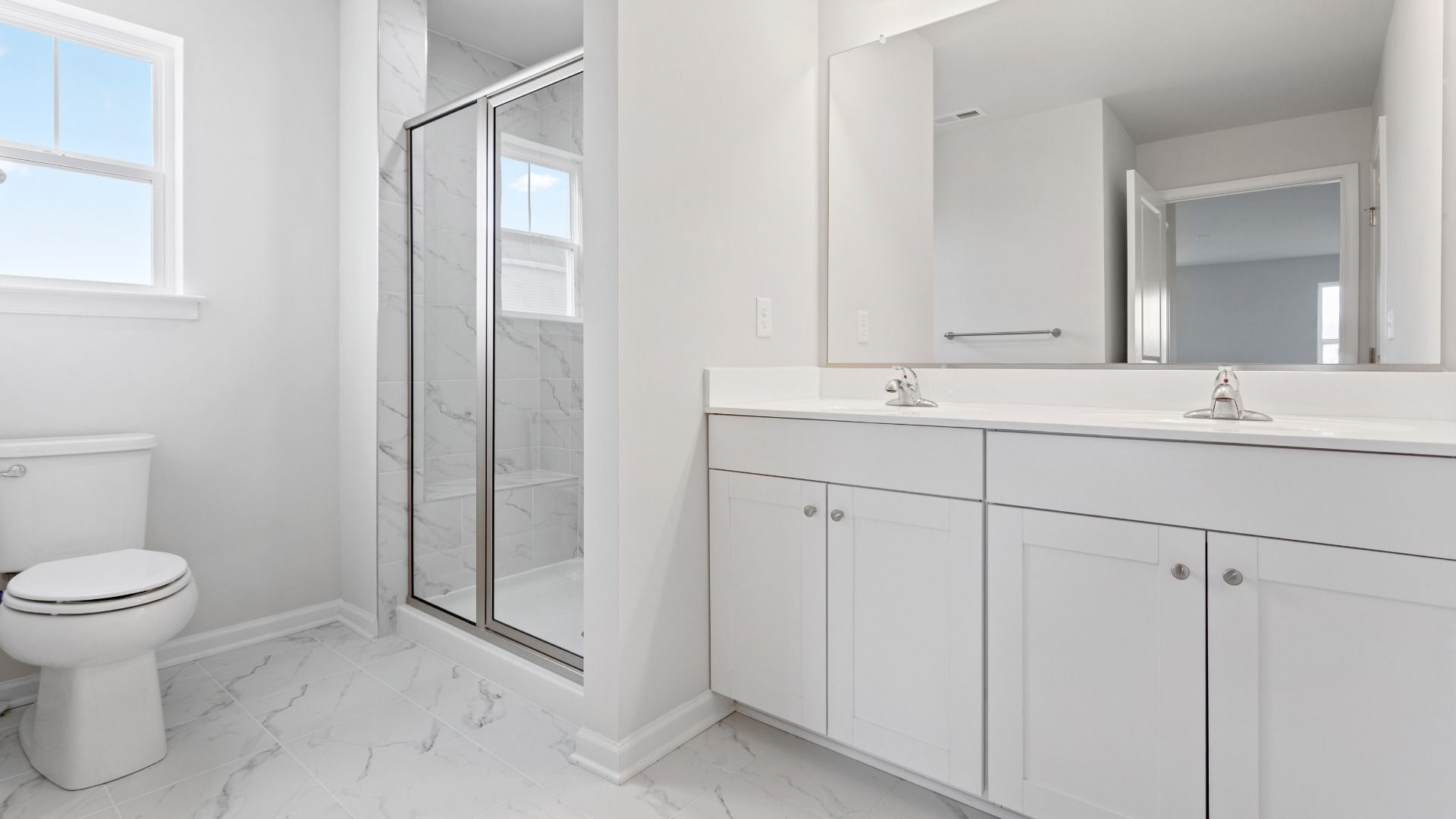 Owner's bath with dual vanity, tiled shower and window in a DRB Homes Edgewood plan at The Village of College Park community.