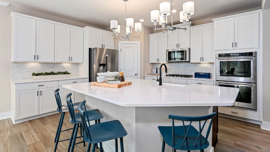 White kitchen with large island, stainless steel appliances in a DRB Homes Barbados model home in The Estuary community.