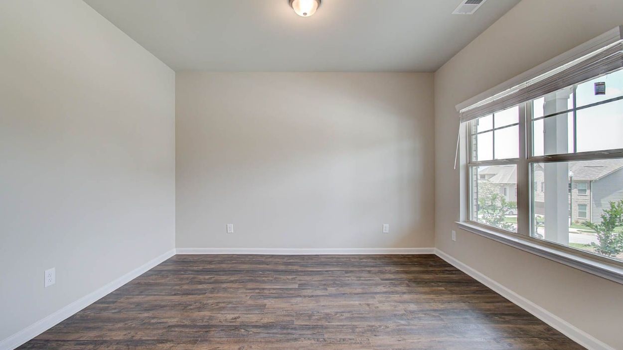 Secondary bedroom with large window, neutral finishes, and LVP flooring in the Vickery at Berkeley Lakes in Locust Grove, GA.