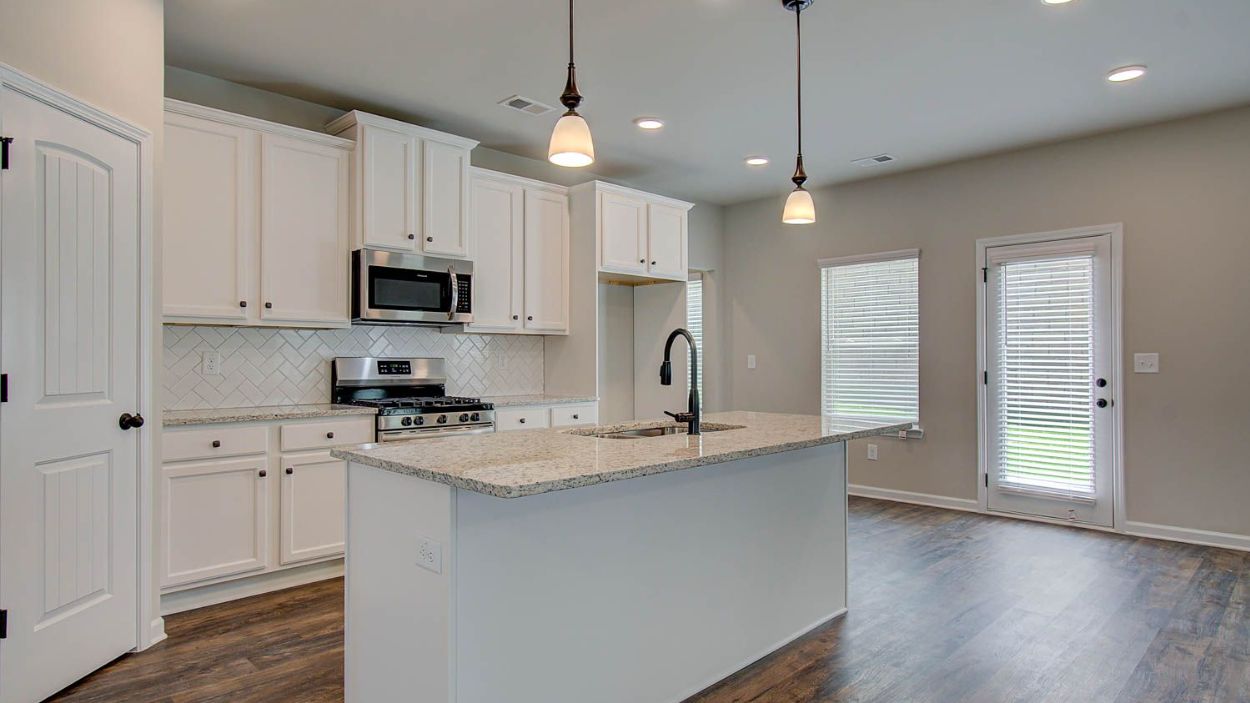 Vickery kitchen with oversized island, white cabinetry and tile backsplash, and pendant lighting at Berkeley Lakes.