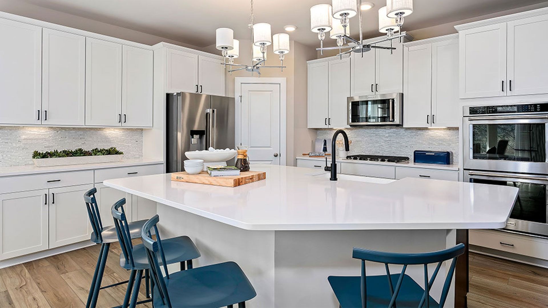 Light and bright kitchen with white cabinets, white counters, large island with sink and stainless steel appliances.