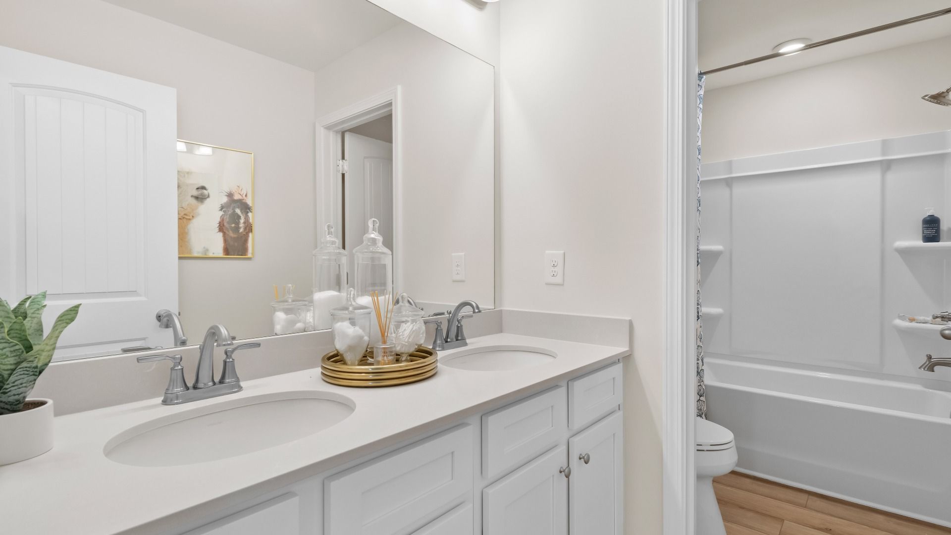 Secondary full bath with dual vanities, shower-tub combo, and LVP flooring in the Wagener at Burchwood in Stockbridge, GA.