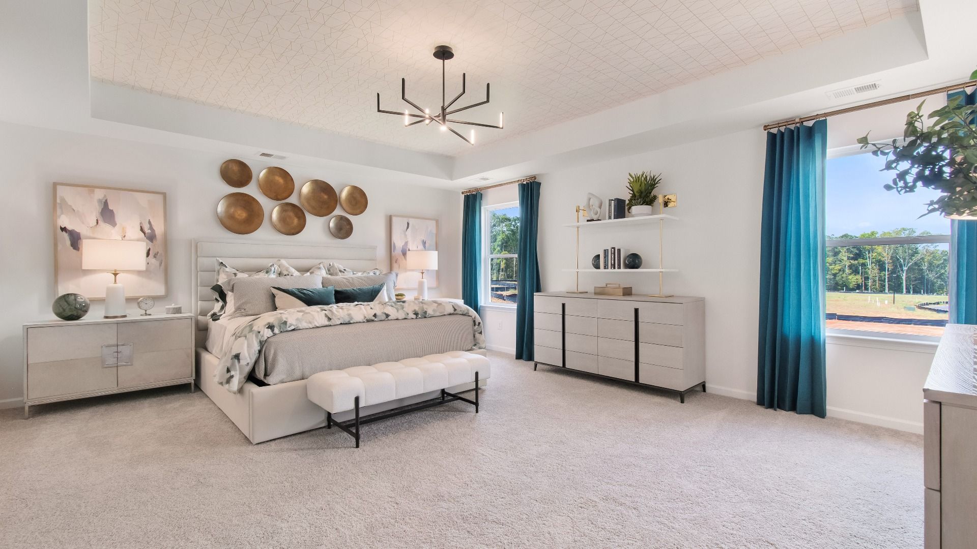 Wagener expansive primary suite with tray ceiling, chandelier lighting, and carpet flooring at Burchwood in Stockbridge, GA.