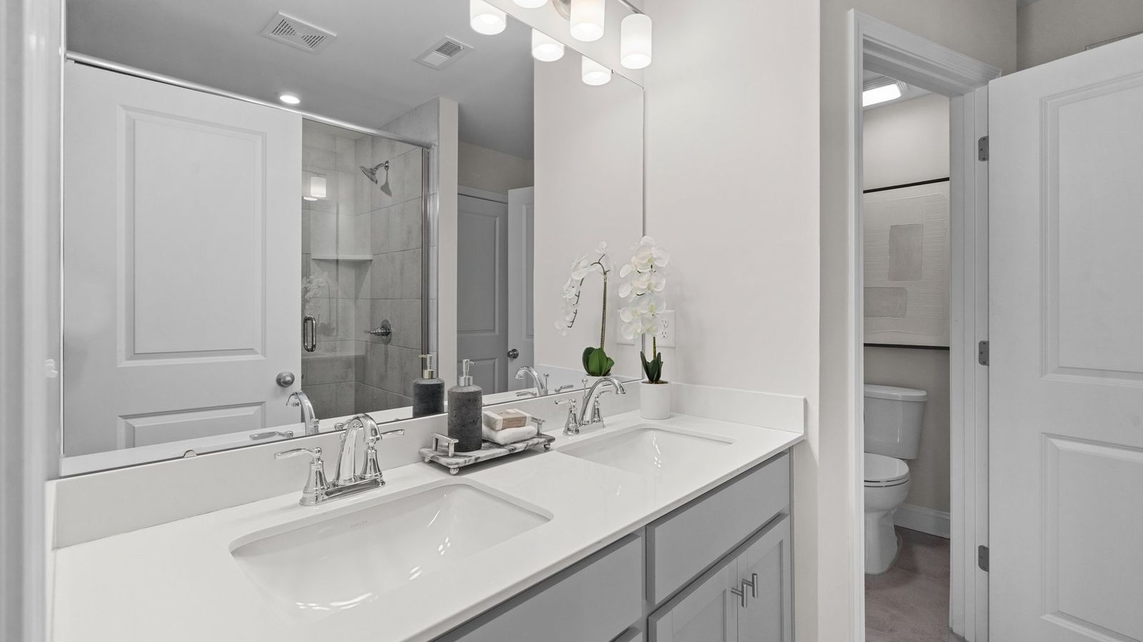The Rochester primary bathroom with dual vanity, fully tiled shower with seat, separate water closet, and premium lighting.