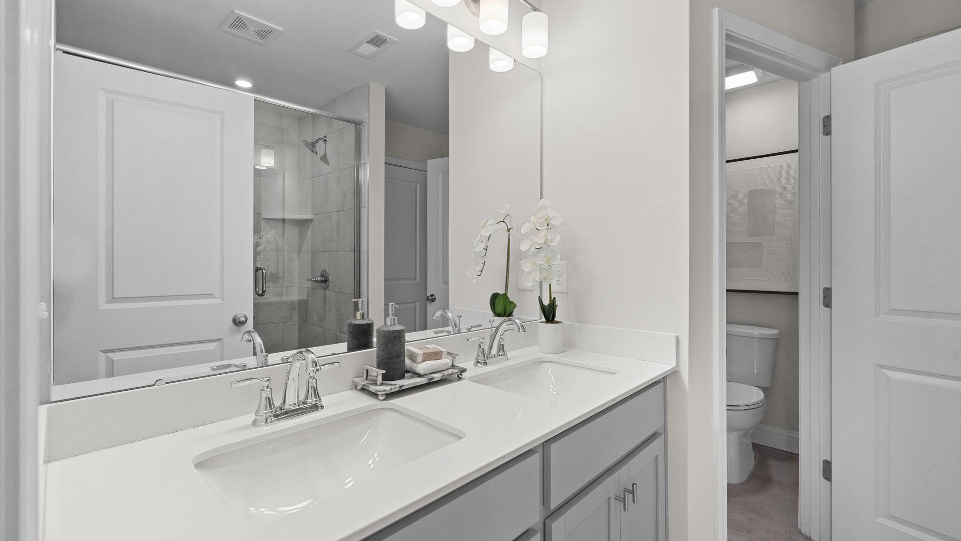 The Rochester primary bathroom with dual vanity, fully tiled shower with seat, separate water closet, and premium lighting.