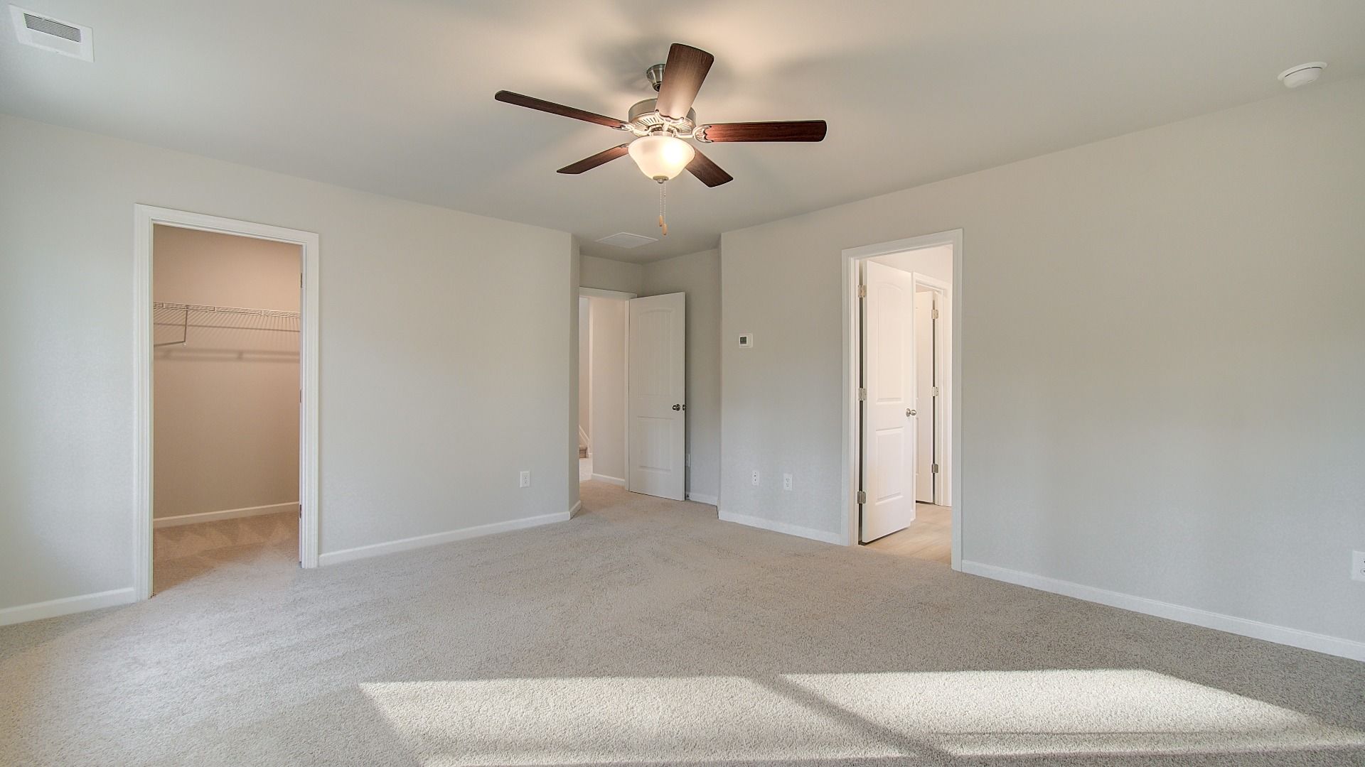 Spacious primary suite featuring carpet flooring with connected closet and bath in the Pelham at Bowers Farm.