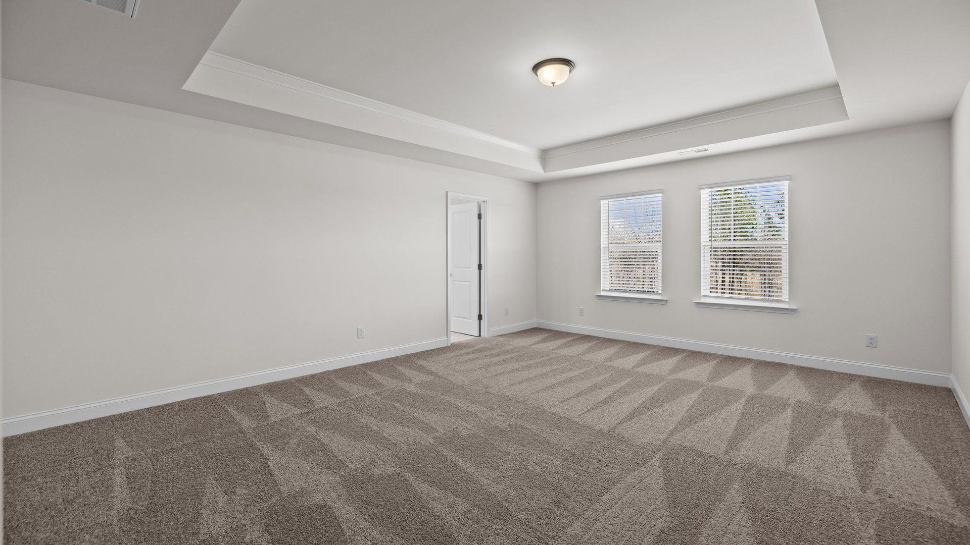 Ample primary bedroom with elevated tray ceiling and plush carpeting, in the Norris Design by DRB Homes in York, SC