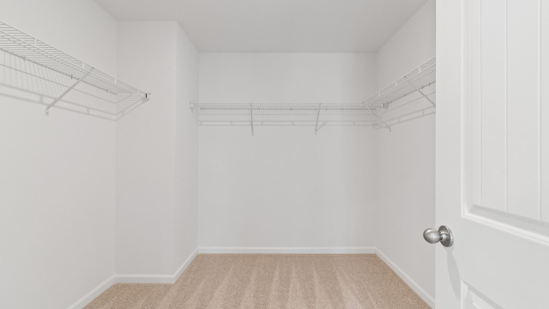 Spacious primary closet with carpet flooring and built-in shelving in the Austin Alternate at Bowers Farm Townhomes.