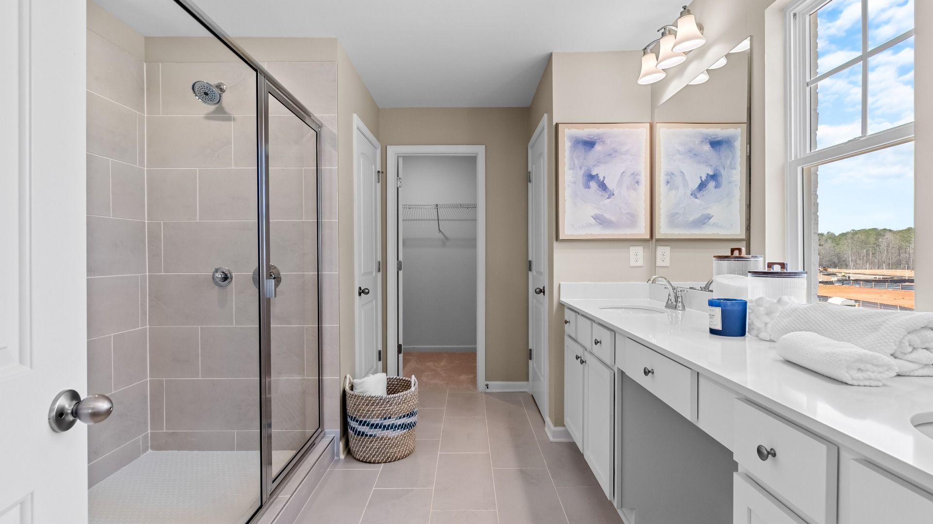 Light-filled primary bath showcasing dual vanities, walk in closet, and sleek neutral detail at Bowers Farm in McDonough, GA.