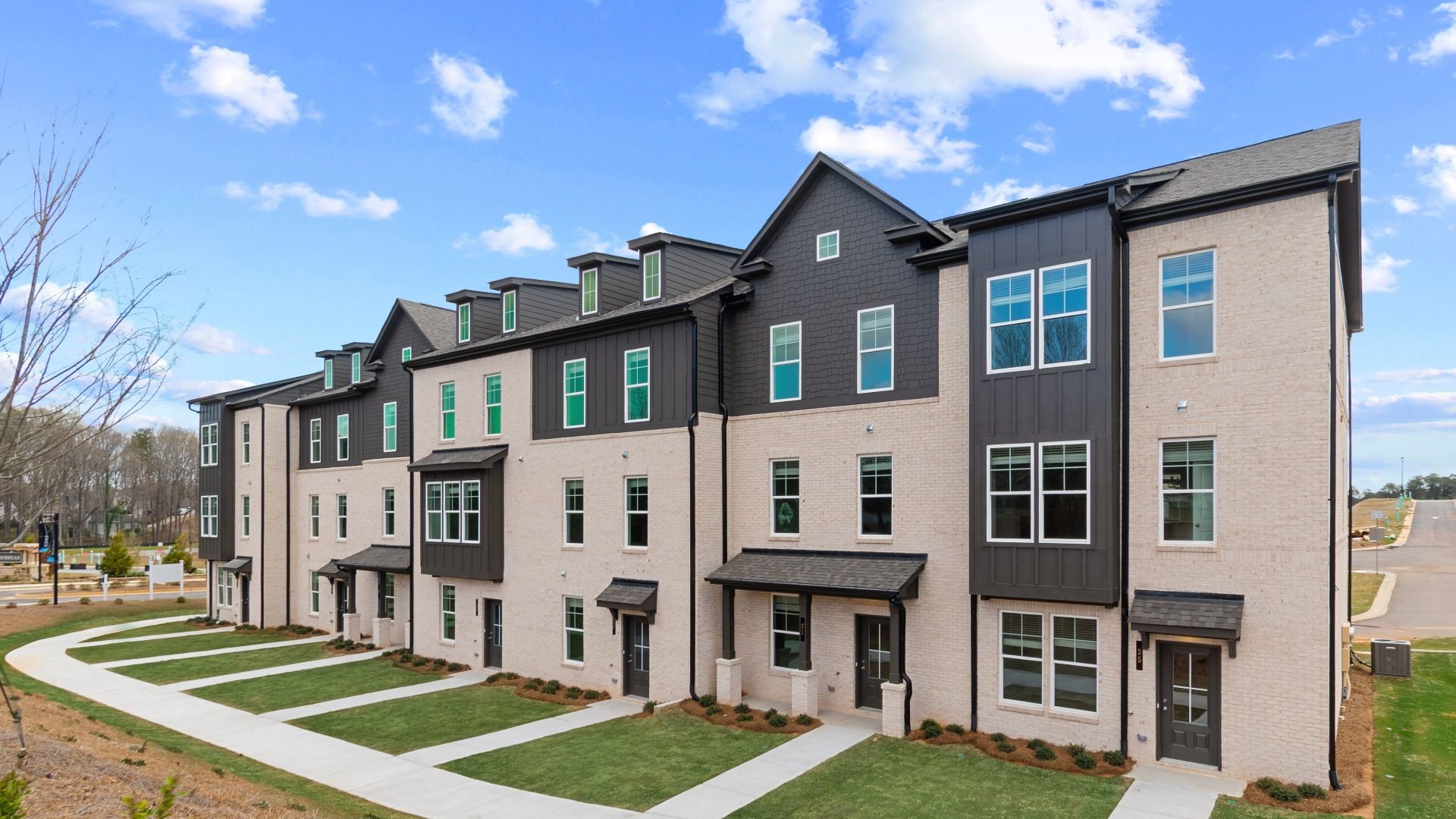 Three-story luxury new construction townhomes with brick and siding exterior features and paved entry ways at Daybreak.