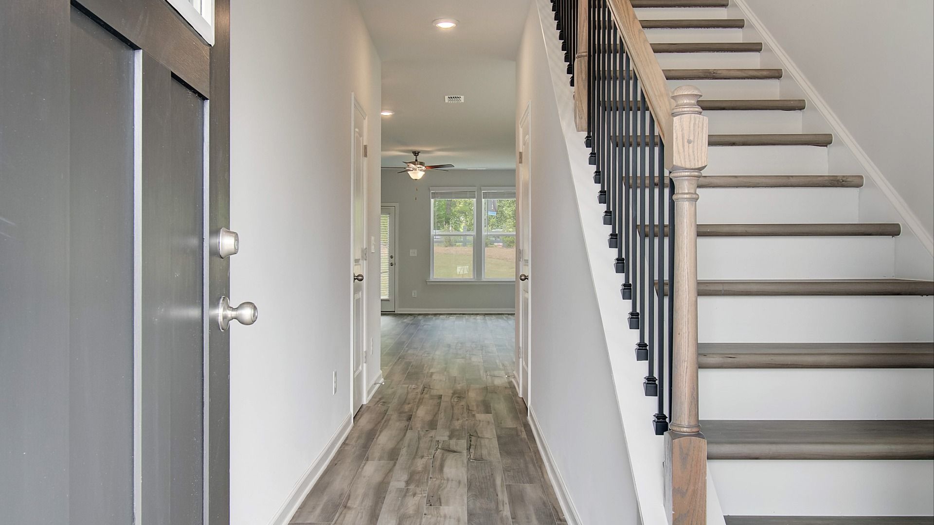 Welcoming foyer with gray front door, LVP floors, staircase with black spindles, and open view to living space.