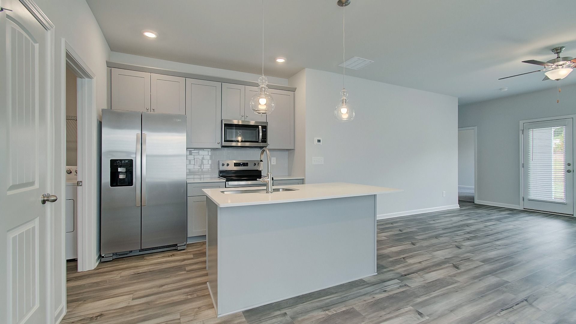 Bright open kitchen featuring center island, grey cabinets, quartz counters, and stainless steel range and microwave.