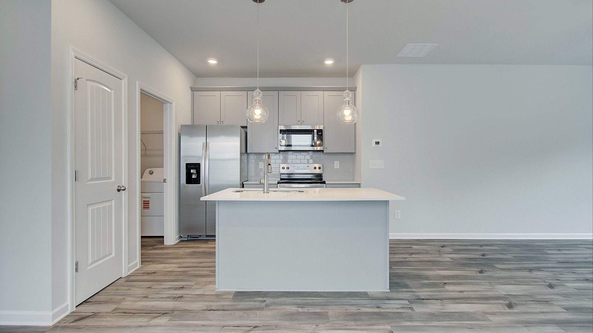 Bright open kitchen featuring center island, grey cabinets, quartz counters, and stainless steel range and microwave.