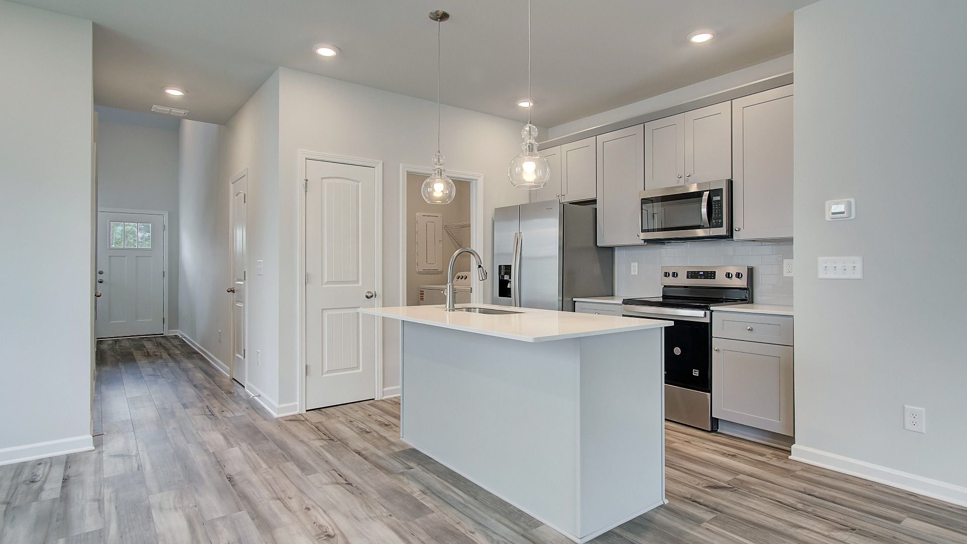 Bright open kitchen featuring center island, grey cabinets, quartz counters, and stainless steel range and microwave.