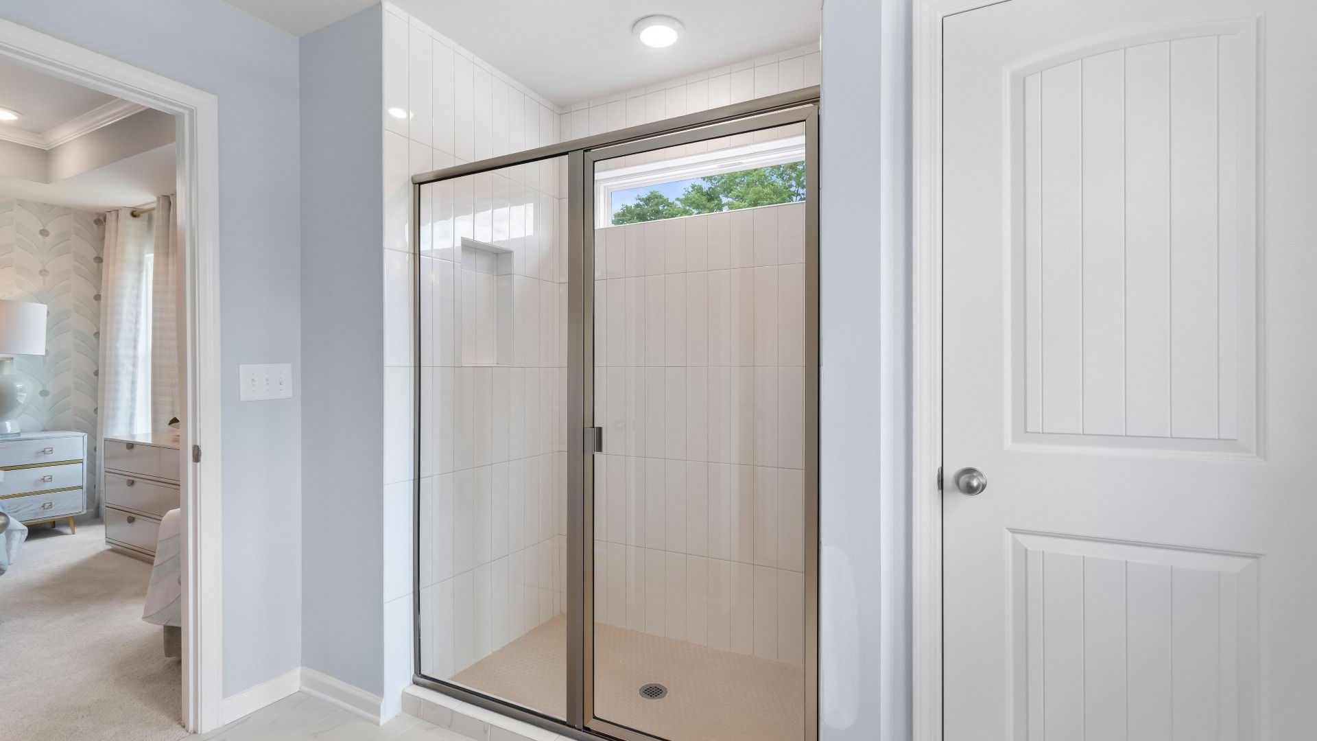 Bright bathroom featuring tile walk-in shower with glass door and sleek finishes in new construction townhome.