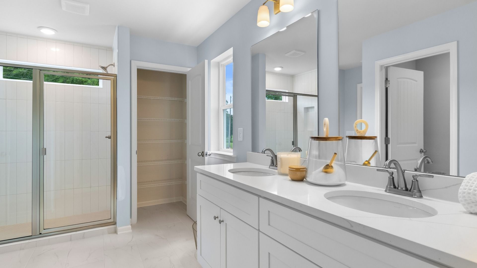 Spacious primary bathroom with double vanity, white quartz countertop, glass walk-in shower, and light blue walls.