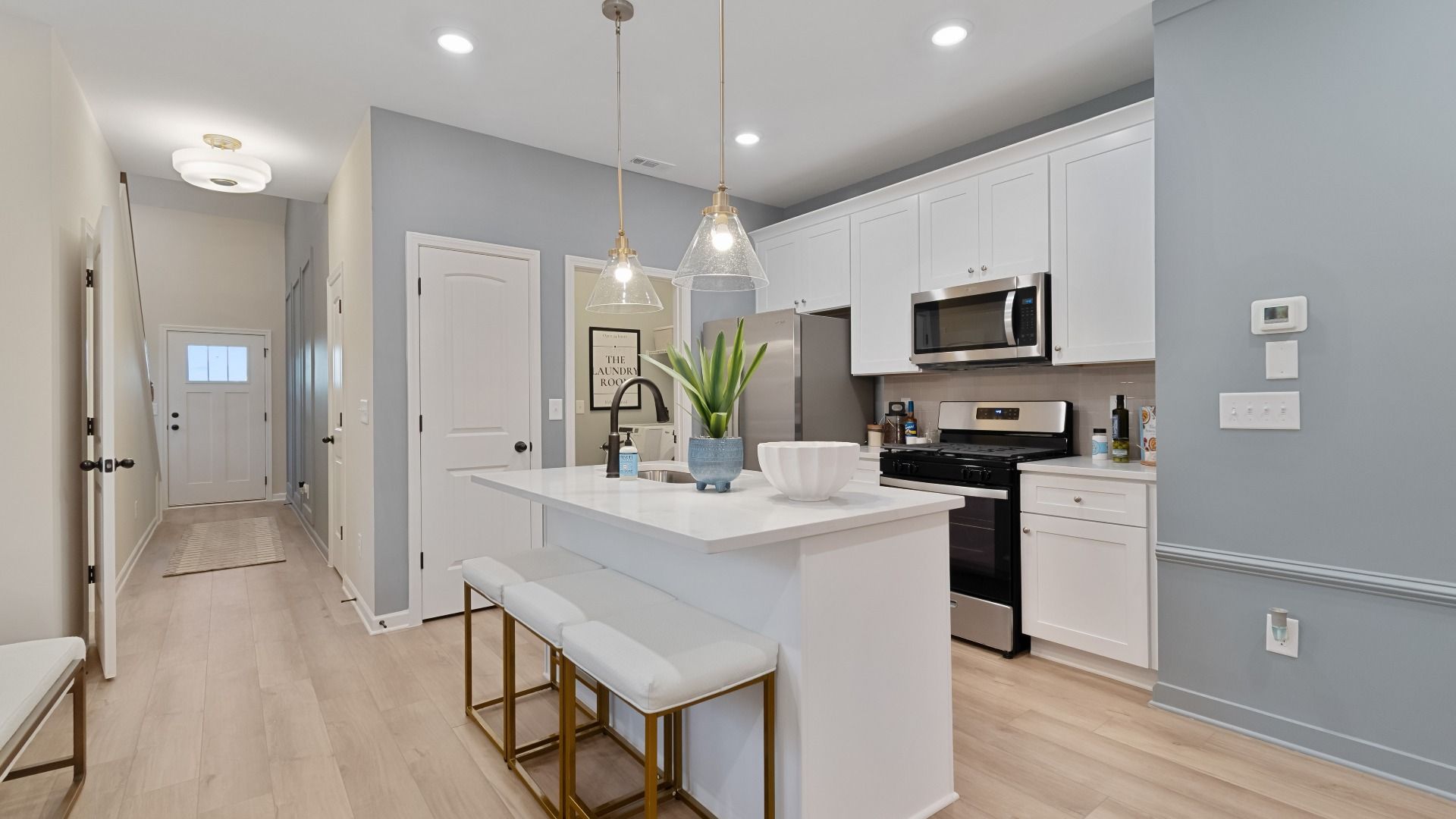 Bright open kitchen featuring center island, white cabinets, quartz counters, and stainless steel range and microwave.