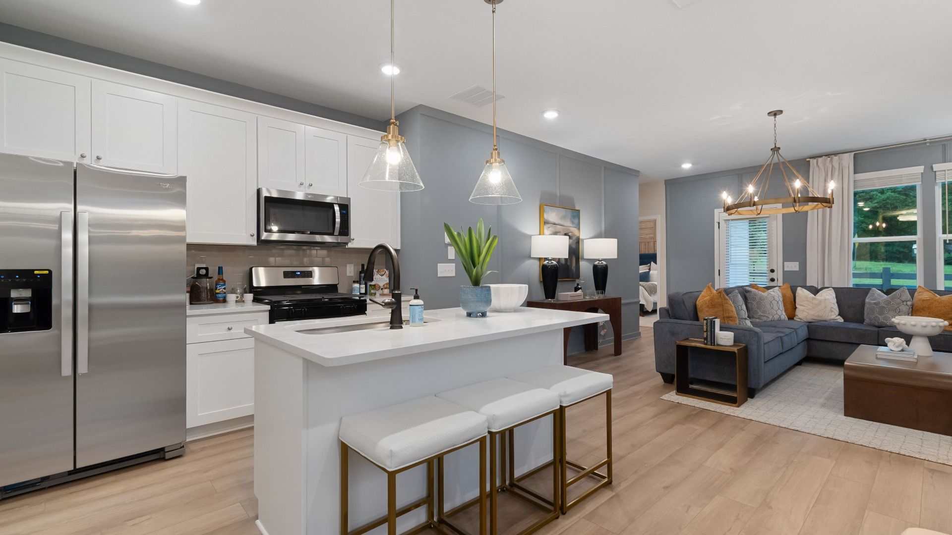 Bright open kitchen featuring center island, white cabinets, quartz counters, and stainless steel range and microwave.