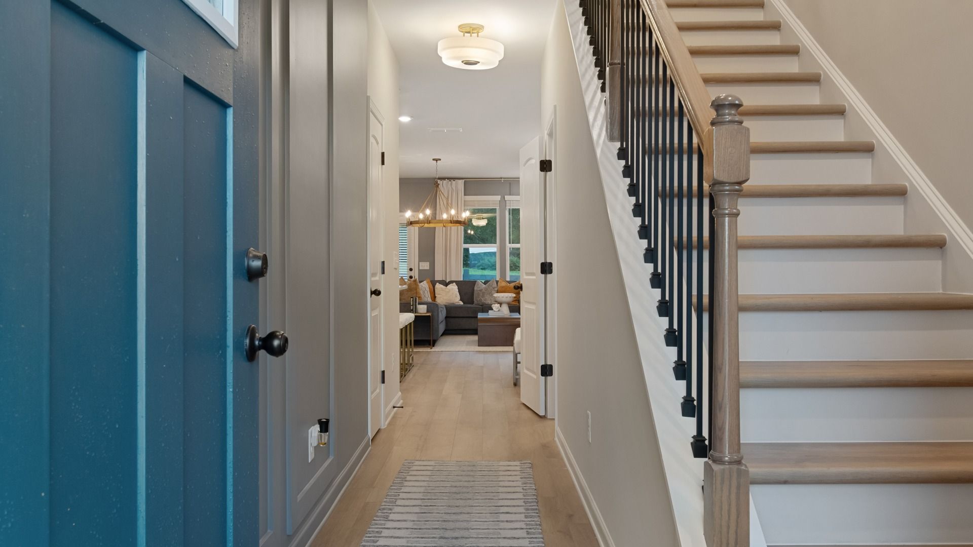 Welcoming foyer with blue front door, LVP floors, staircase with black spindles, and open view to living space.