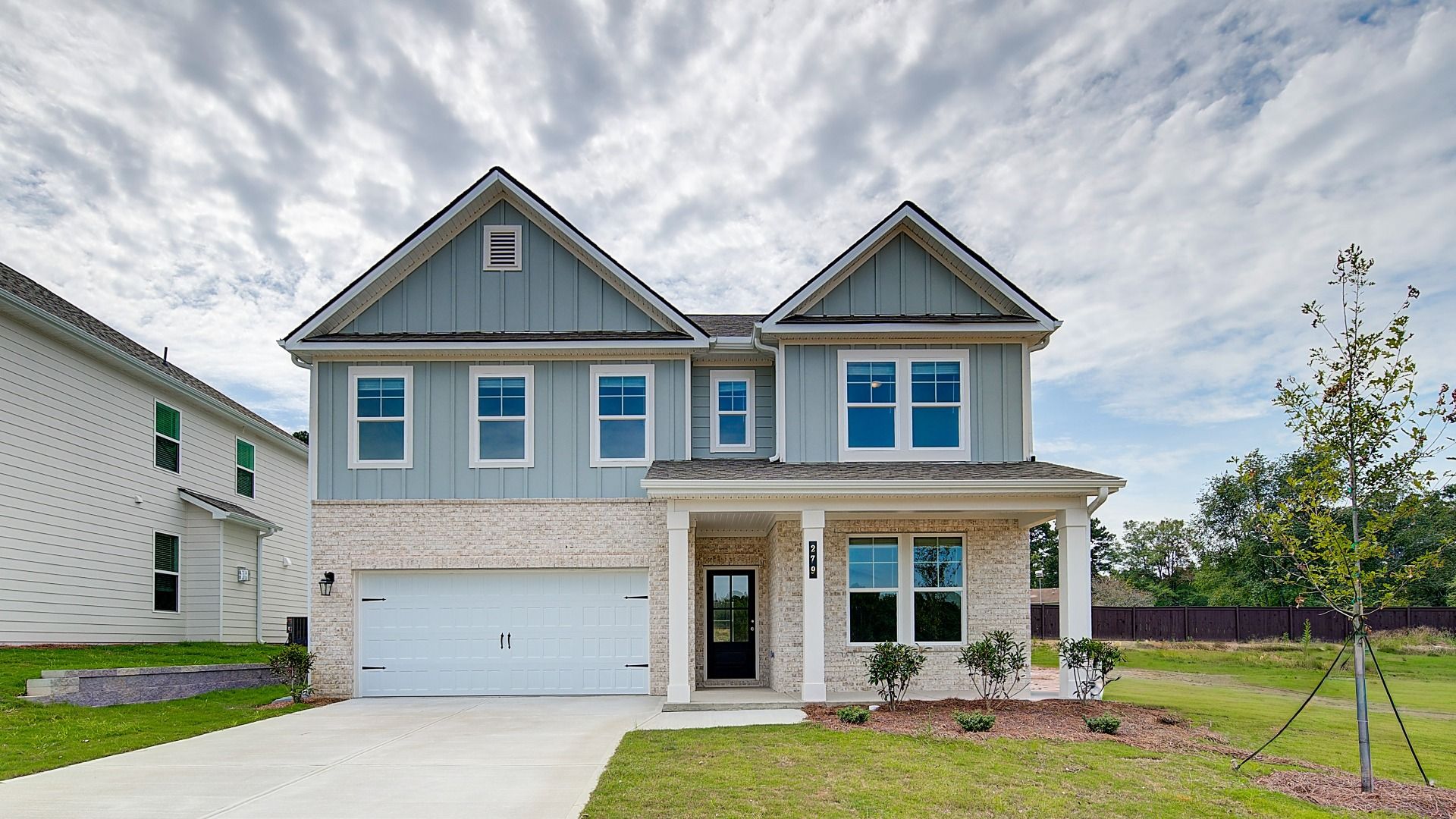 Two-story new home with white columns, tan brick exterior, and light green fiber cement accents in Abbotts Crossing.