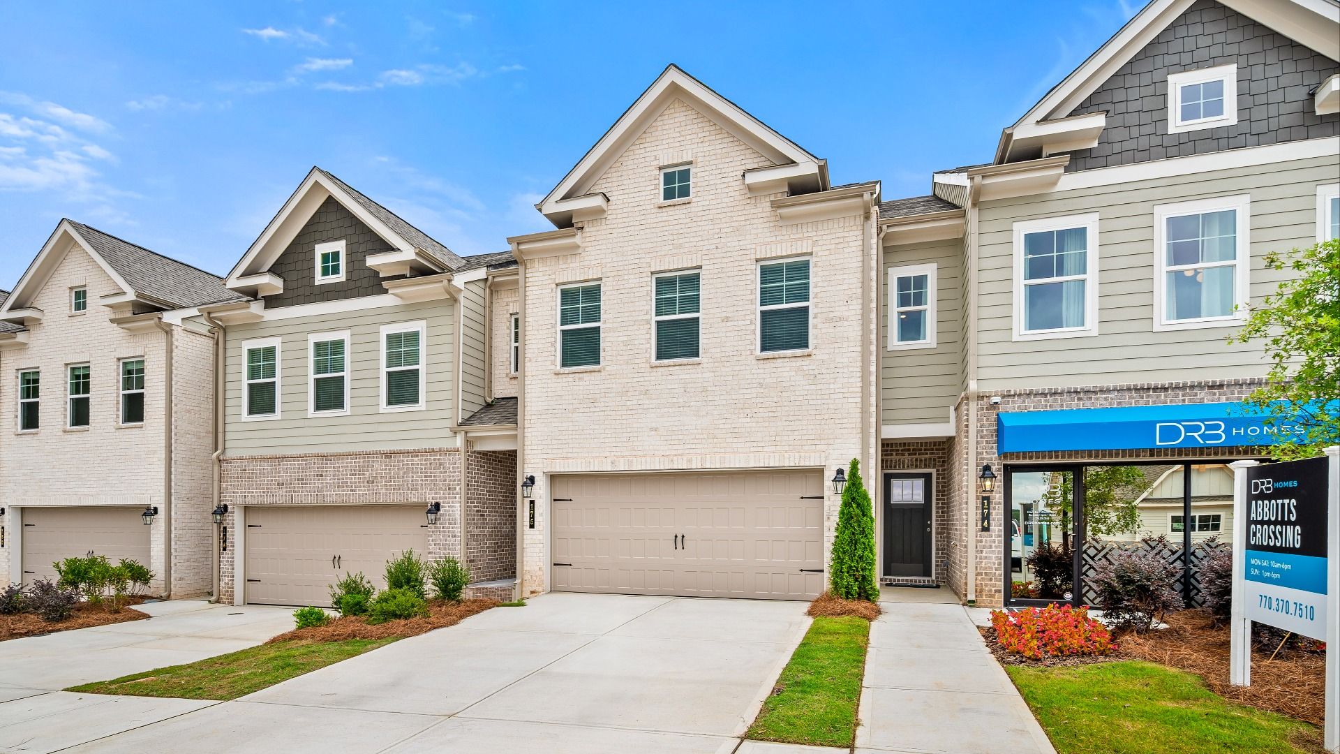 Row of modern 2-car garage townhomes with light tan brick, soft sage fiber cement siding, and dark gray shake accents.