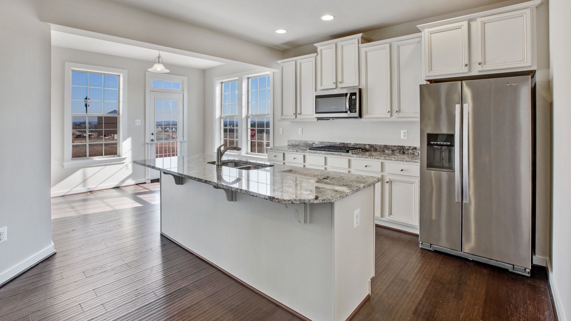 White open kitchen with large island with sink, stainless steel appliances and recessed lights.