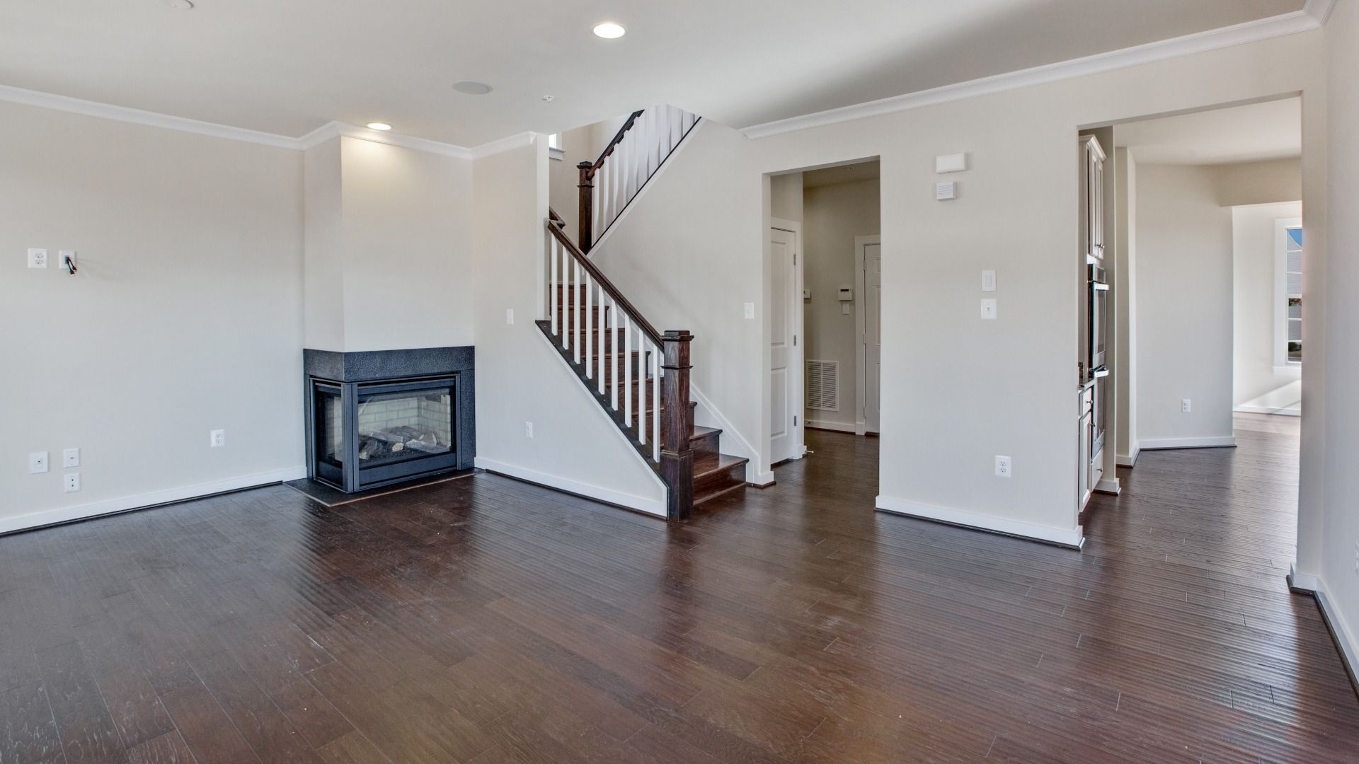 Spacious living room with medium toned wood floors, corner fireplace and recessed lighting.