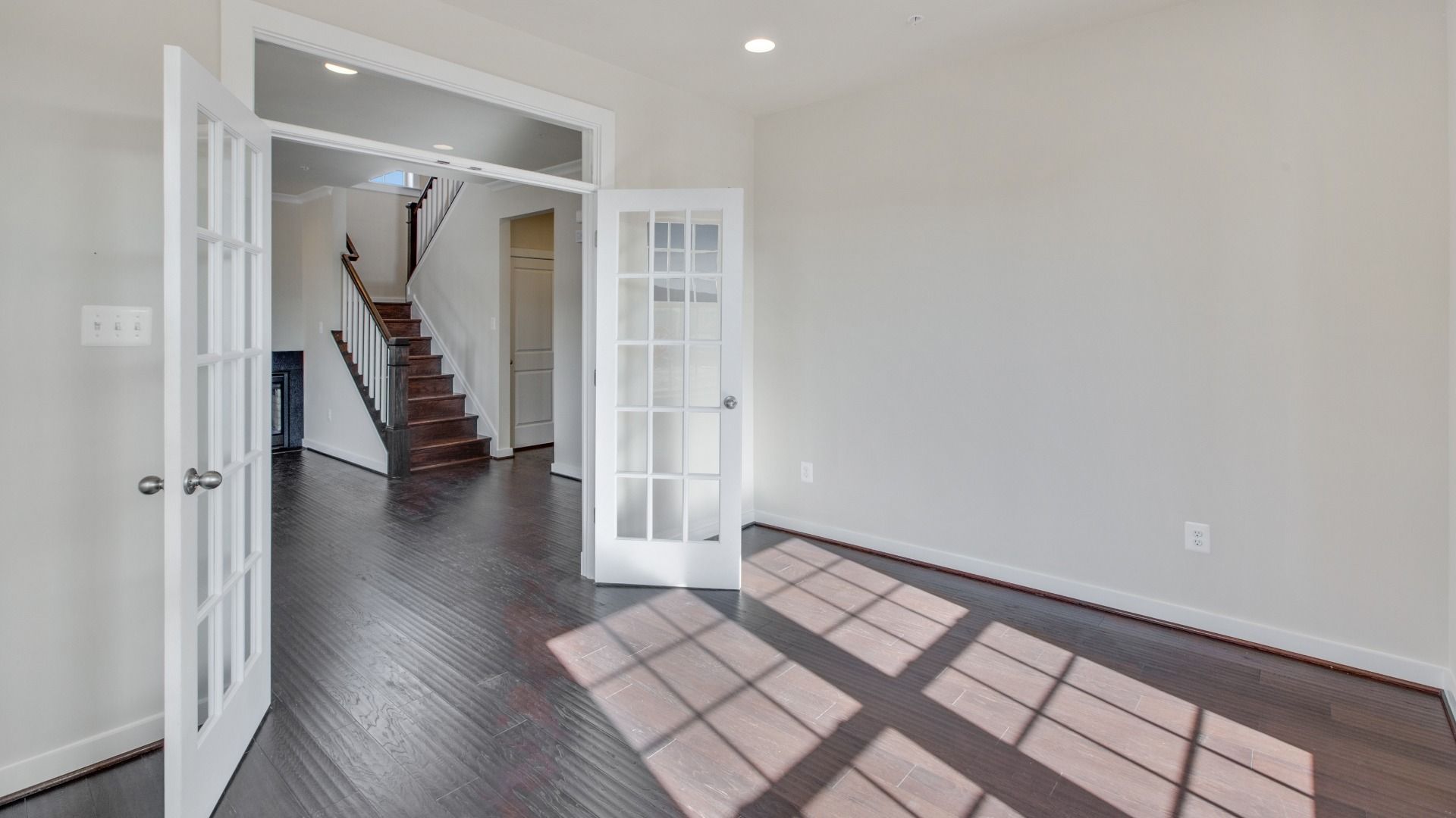 Light and bright study with French doors and transom, large double window, medium toned wood floors, recessed lighting.