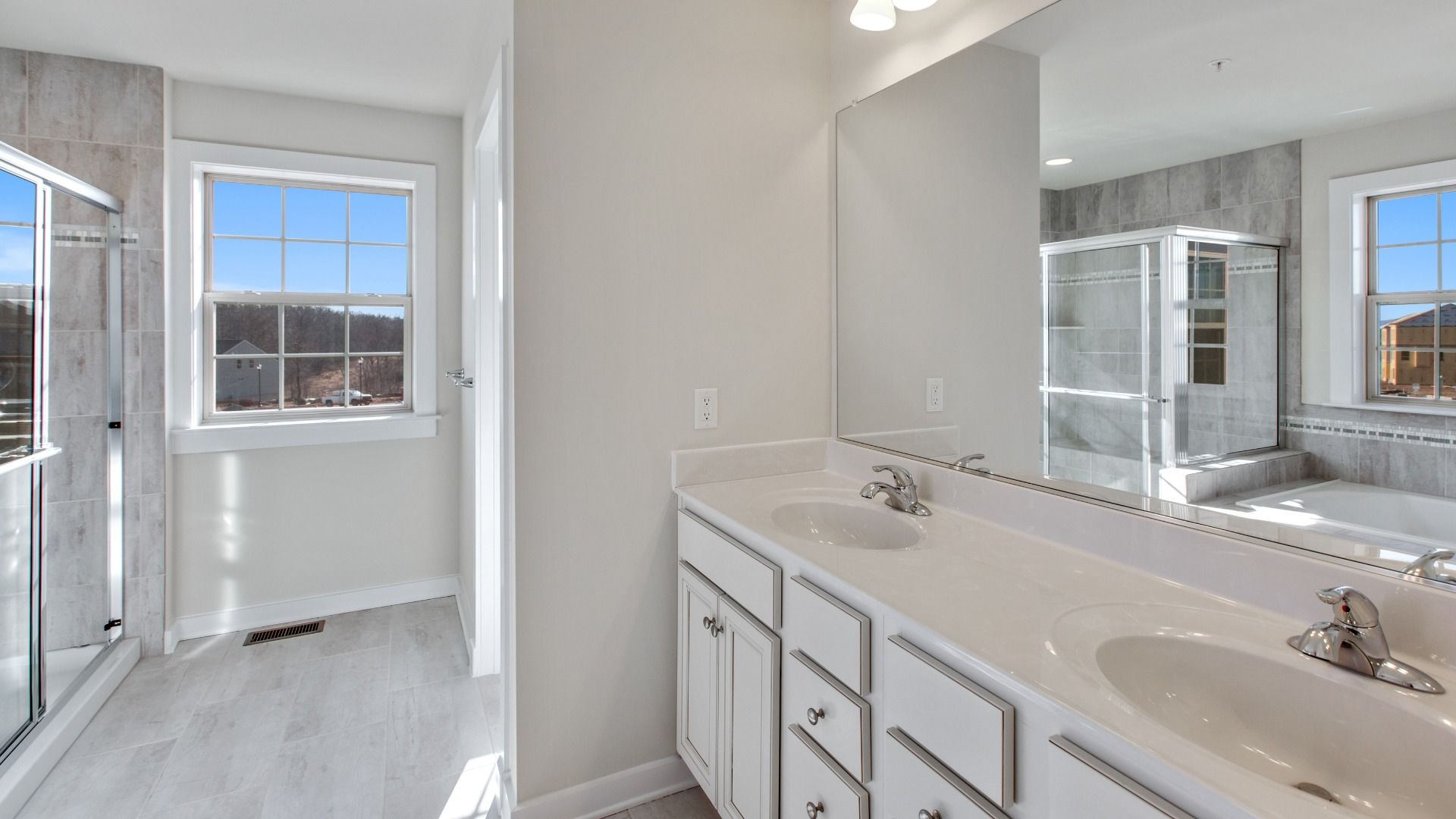 Large owner's bathroom with dual sink vanity, white cabinets and counters, walk-in shower and large window.