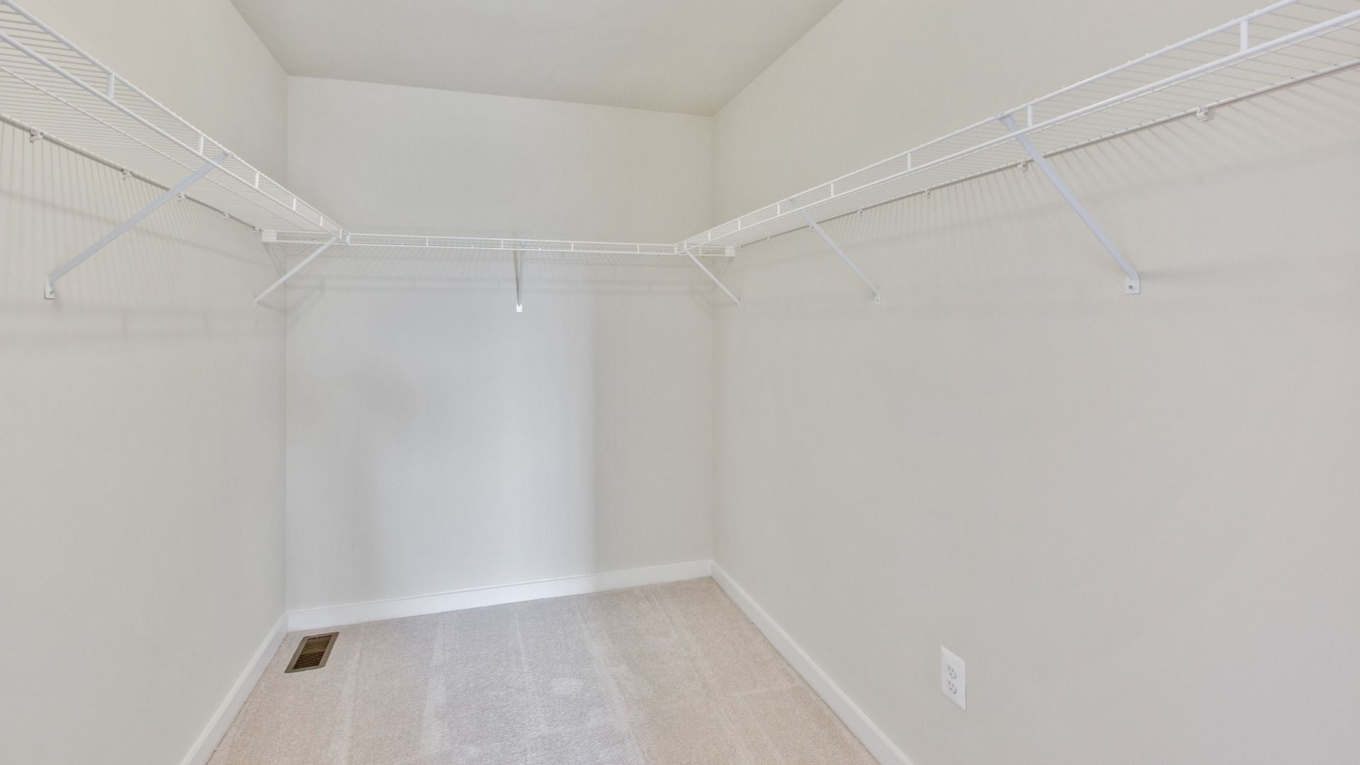 Generous owner's suite walk-in closet with wall to wall carpet and white wire racks on 3 walls.