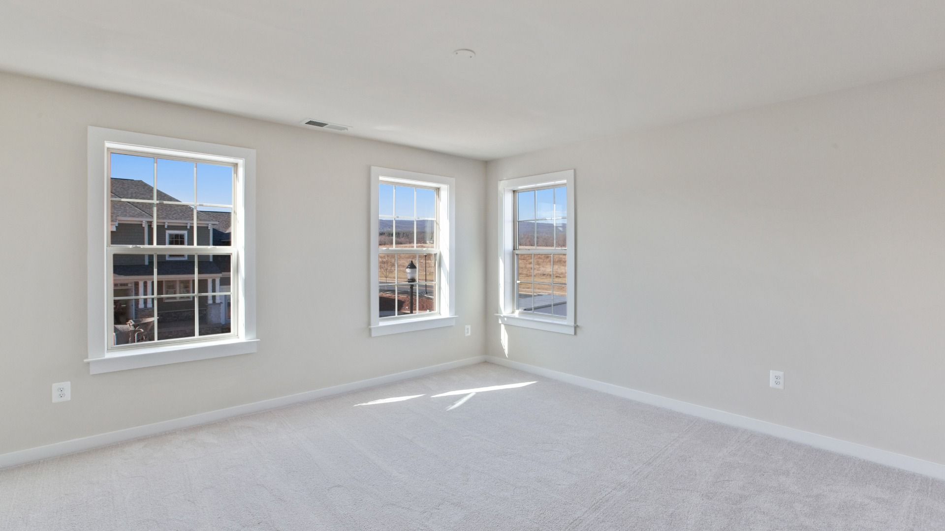 Large secondary bedroom with light colored wall to wall carpet and 3 large windows on adjacent walls.