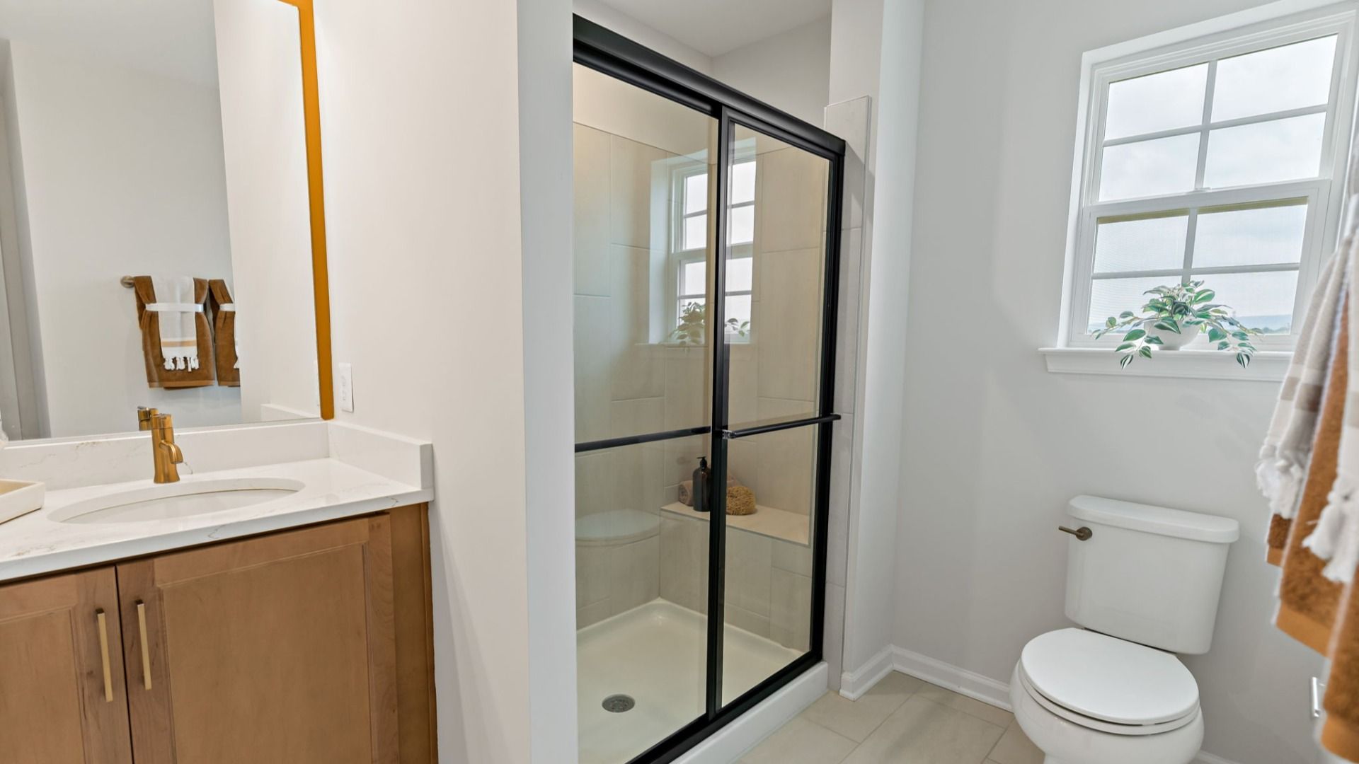 A sleek owner’s bath featuring a glass shower and a bright window in the Edgewood II.
