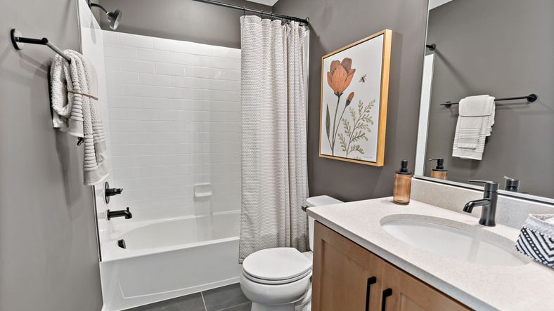 Bathroom with a tub, shower, white towels, and framed botanical artwork in the York II Garage floor plan.