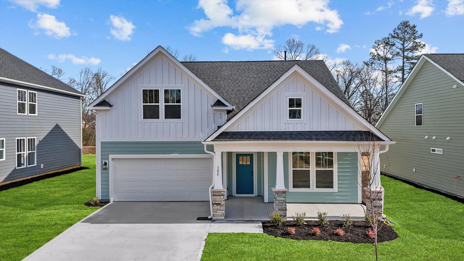 Two toned, neutral exterior home with red door, front porch, two car garage, and stone columns at DRB Homes in Greenville, SC